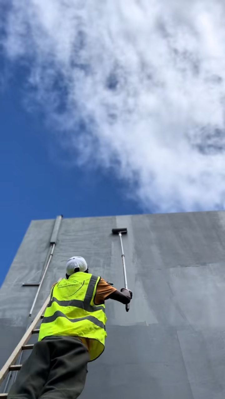 Ouvrier sur une échelle appliquant le Polylastic en haut de la façade