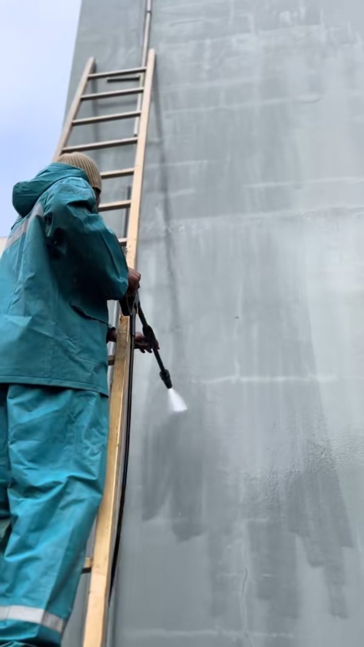 Ouvrier en tenue de pluie nettoyant la façade au jet haute pression