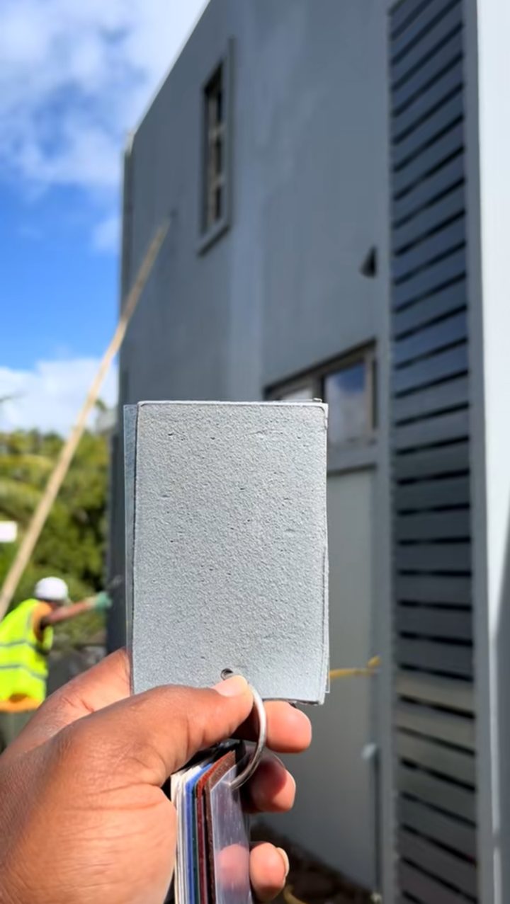 Échantillon de couleur tenu devant la façade terminée pour comparer la teinte